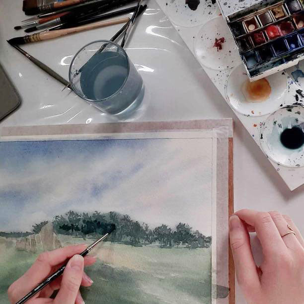 Emma de Morel, une artiste peintre normande actuelle peint un tableau d'un paysage de Normandie à l'aquarelle.