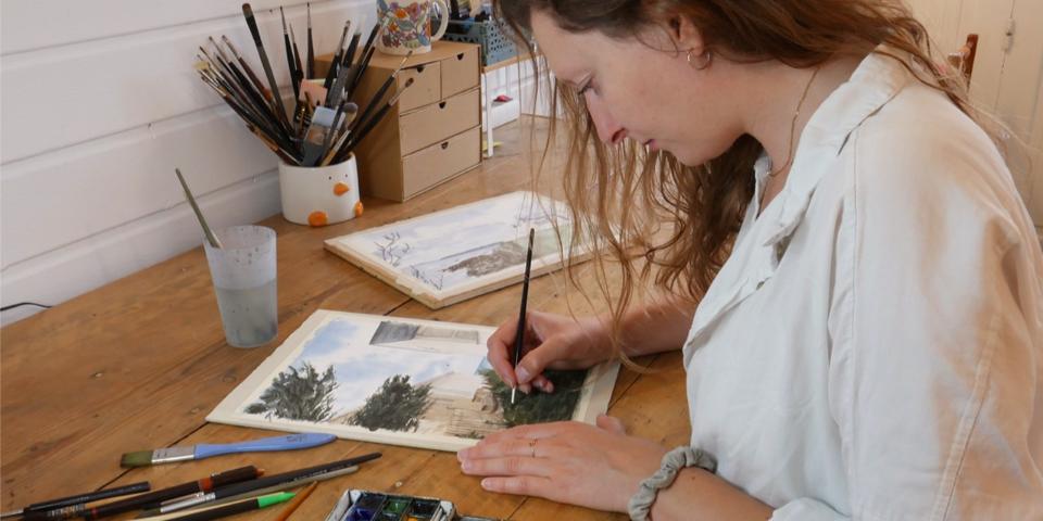 artiste dans son atelier qui peint une aquarelle de maison de famille